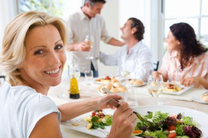 Four friends having lunch at table, woman serving herself salad in foreground, smiling, portrait